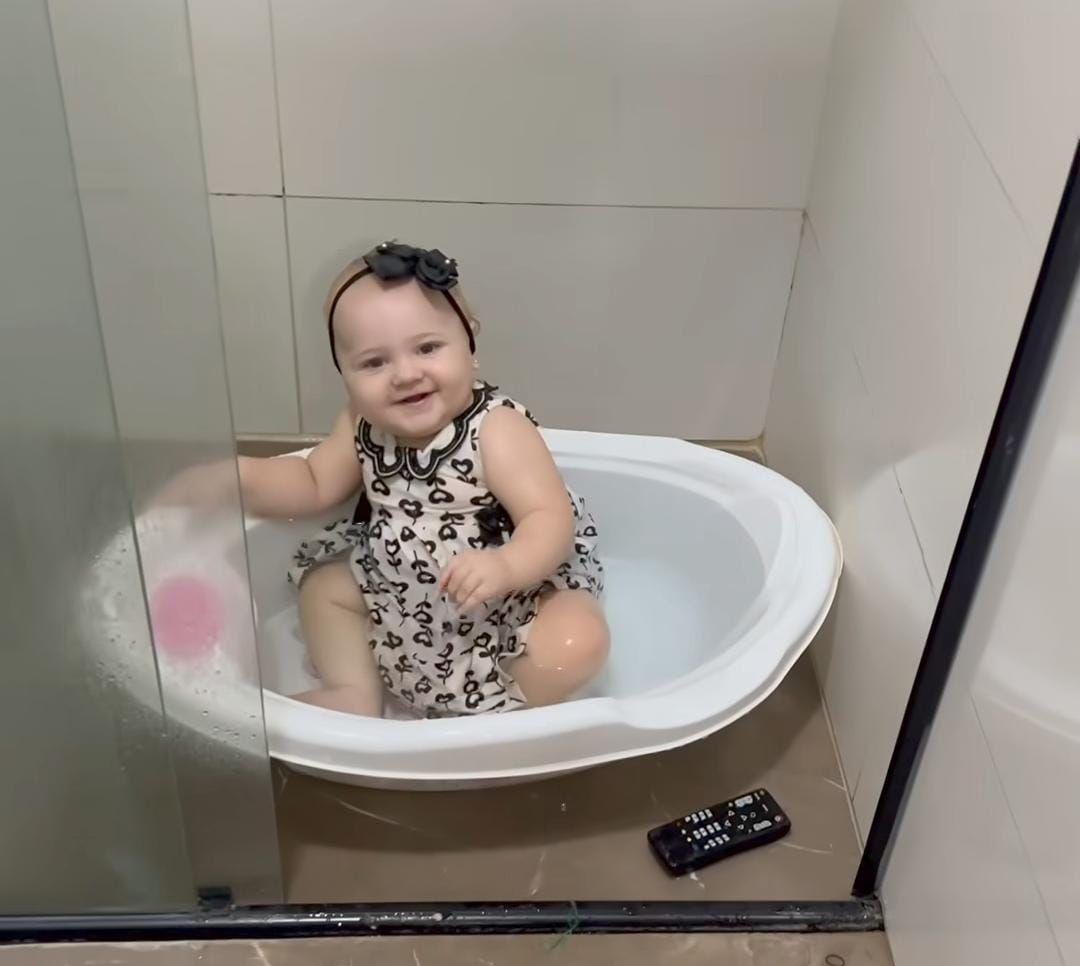 Imagem - Bebê rouba a cena ao entrar totalmente vestida em banheira enquanto mãe se distrai