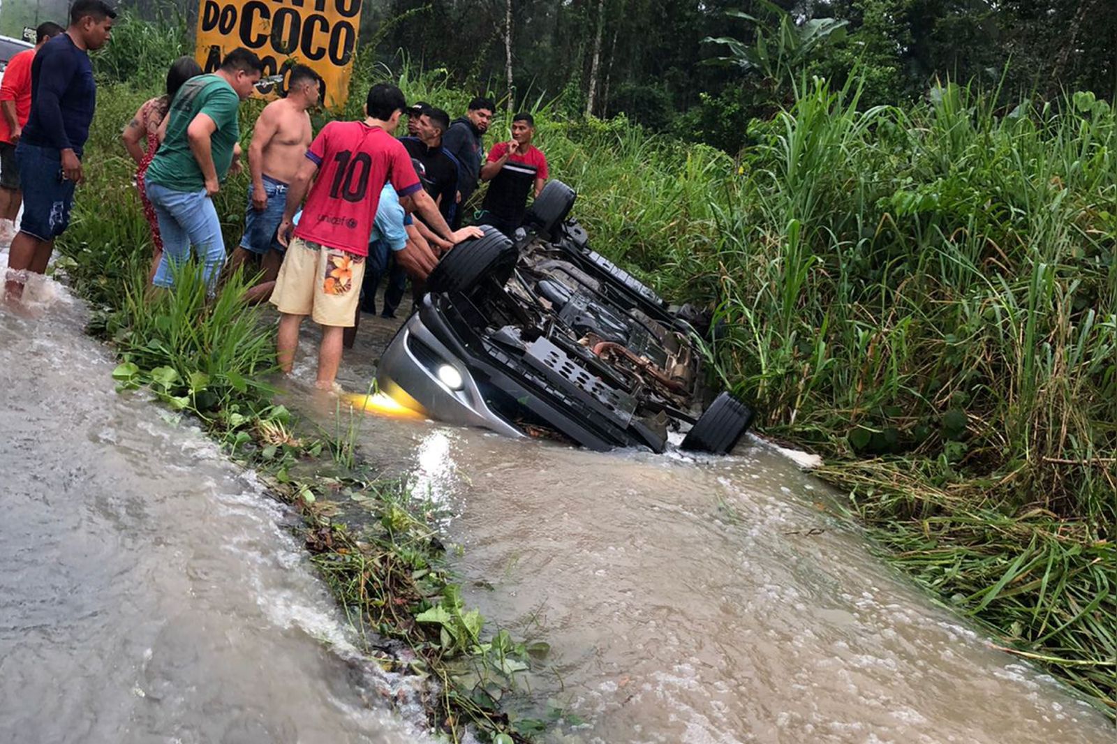Um motorista perdeu o controle de um carro de passeio, após passar por um buraco. O carro capotou e foi parar em um córrego às margens da via.