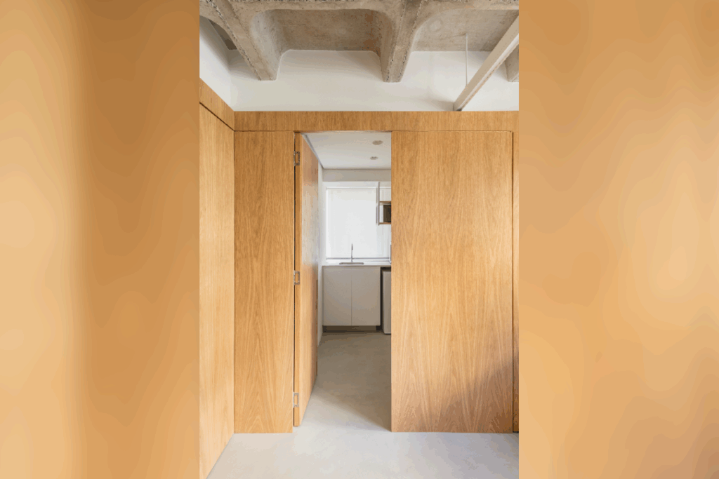 Portas camufladas em painéis de madeira otimizam o espaço e reforçam a sofisticação da marcenaria planejada (Projeto: Escritório Conectarq | Imagem: Guilherme Pucci)