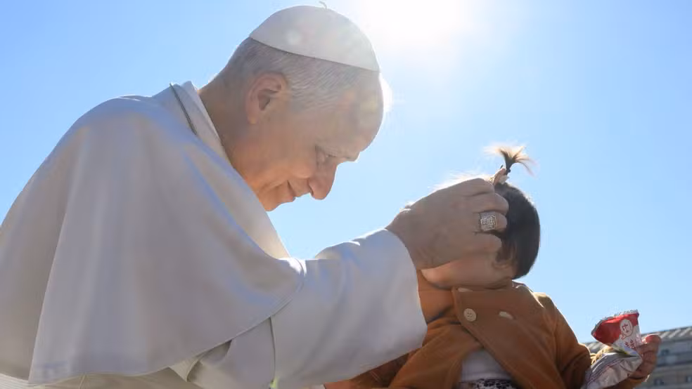 (O pontífice a segurou no colo e proferiu uma bênção diante de milhares de fiéis.)